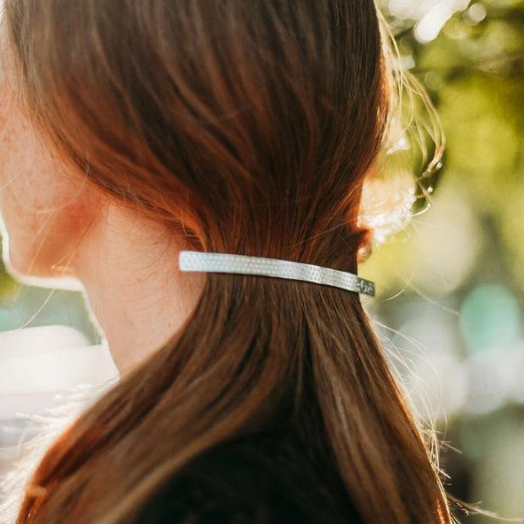 FEMME DONT LES CHEVEUX SONT RETENUS PAR UNE LONGUE ET FINE BARRETTE ARGENTEE E AVEC DECOR PETITES FLEURS GRAVEES