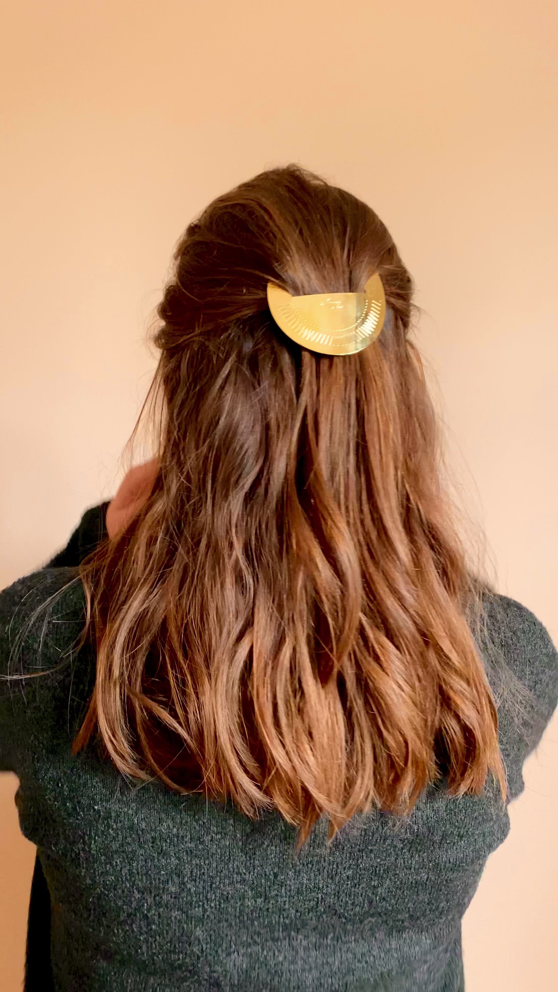 Femme aux cheveux longs portant une demi queue ornée d'une barrette dorée ronde